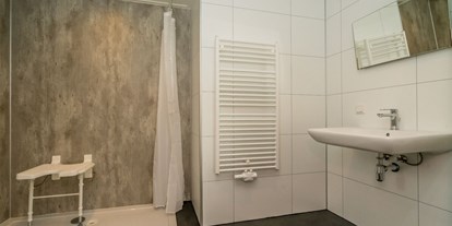Rollstuhlgerechte Unterkunft - See - Niederlande - Die Dusche hat einen Sitz und Haltegriffe, einen unterfahrbaren Waschtisch und einen höhenverstellbaren Spiegel. Das Dusch-WC hat klappbare Stützen. Im Flur des Hauses befindet sich noch eine separate Toilette. - Rollstuhl Urlaub in Zeeland - De Klaproos