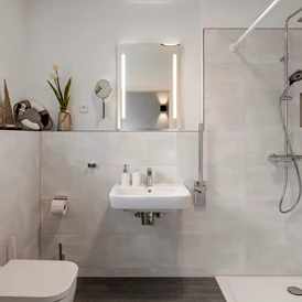 Rollstuhl-Urlaub: Badezimmer im Erdgeschoss mit unterfahrbarem Waschbecken inkl. Haltestange, WC inkl Haltestange und ebenerdiger, befahrbarer Dusche (120x120cm) mit Duschstange und Duschhocker - Haus Fichte