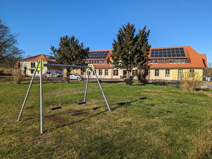 Rollstuhlgerechte Unterkunft - Pflegebett - Spiel und Bewegung im Grünen – Der Park des Gutshofes Roggow
Vor der historischen Kulisse des Gutshofes Roggow erstreckt sich eine weitläufige Rasenfläche, die Kindern und Jugendlichen vielfältige Spiel- und Sportmöglichkeiten bietet. Ein moderner Spielplatz mit Seilbahn, Trampolin, Schaukel und Kleinkinderwippe lädt zum Toben ein, während der Volleyballplatz und der kleine Bolzplatz auch ältere Kinder und Erwachsene zu gemeinsamen Aktivitäten animieren.
Hier finden Feriengäste wie auch Bewohner mit Besuch von Kindern einen idealen Ort, um in sicherer Umgebung frische Luft und Bewegung zu genießen – eingebettet in die gepflegte Parklandschaft des Gutshofes. - Gutshof Roggow bei Güstrow