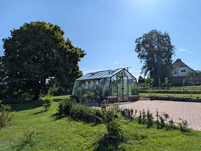 Rollstuhlgerechte Unterkunft - Pflegebett - Ein Park zum Verweilen – Die grüne Oase des Gutshofes Roggow
Rund um den Gutshof Roggow erstreckt sich eine liebevoll gestaltete Parkanlage, die mit ihrem alten Baumbestand und weitläufigen Wiesen zum Innehalten einlädt. Das Gewächshaus mit gemütlicher Sitzecke für kühlere Tage, eine idyllische Schafweide, ein kleiner Teich und die artenreiche Streuobstwiese sowie die professionell angelegten Staudenbeete verleihen dem Park seinen besonderen Charakter. Gepflegte Wege führen vorbei an sonnigen und schattigen Plätzen, während zahlreiche Sitzbänke Gelegenheit bieten, den Blick über die mecklenburgische Landschaft schweifen zu lassen.
Ein Ort, der Ruhe schenkt und zugleich Raum für Begegnung und Naturerlebnis bietet – für unsere Feriengäste ebenso wie für Besucher des Gutshofes. - Gutshof Roggow bei Güstrow
