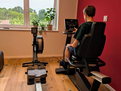 Rollstuhlgerechte Unterkunft - Pflegebett - Aktiv bleiben – Das Fitnesscenter im Gutshof Roggow
Das hauseigene Fitnesscenter steht allen Gästen und Bewohnern kostenfrei zur Verfügung und bietet hochwertige Geräte für ein umfassendes Training: Crosstrainer, Bike und Kraftstation von Technogym, die bewährte Rudermaschine von Concept2 sowie Sprossenwand und Freihanteln. Abgerundet wird das Angebot durch einen Massagesessel – ideal zur Entspannung nach dem Training. Große Fenster sorgen für einen hellen, freundlichen Raum mit Blick ins Grüne. - Gutshof Roggow bei Güstrow