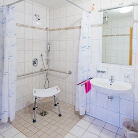 Rollstuhl-Urlaub: Rollstuhlgerechtes Badezimmer mit ebenerdiger Dusche und Duschstuhl - Apartmenthaus Bad Bellingen