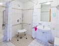 Rollstuhl-Urlaub: Rollstuhlgerechtes Badezimmer mit ebenerdiger Dusche und Duschstuhl - Apartmenthaus Bad Bellingen