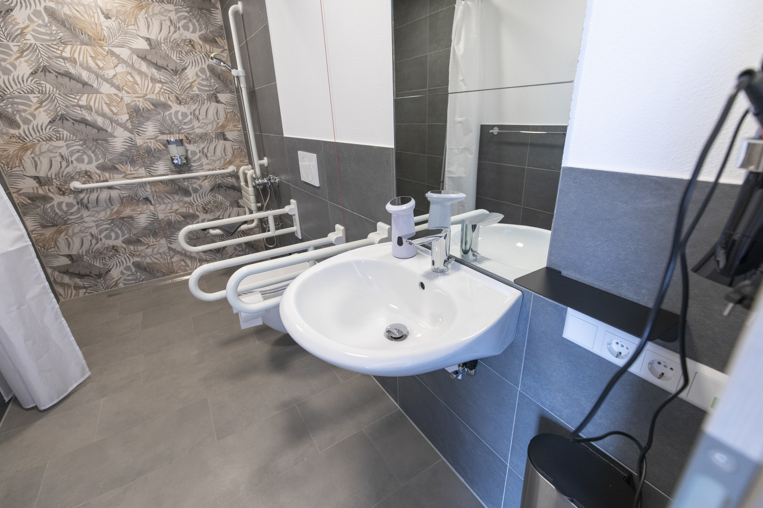 Rollstuhl-Urlaub: Barrierefreies Badezimmer mit Waschbecken, Haltegriffen und großzügiger Dusche. Die moderne Ausstattung ermöglicht eine komfortable Nutzung auch für Gäste mit eingeschränkter Mobilität. - Pension Alter Hirsch - Ferienwohnung Tanne