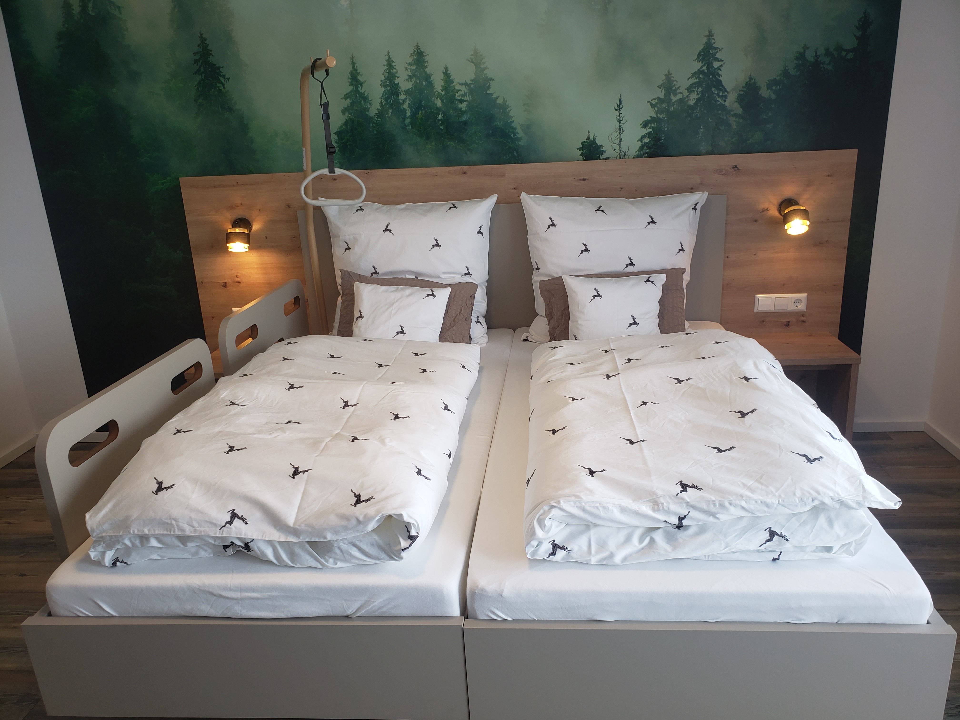 Rollstuhlgerechte Unterkunft - Barrierefreiheit-Merkmale: Für Gäste mit Gehbehinderung oder Rollstuhlfahrer - Schwarzwald - Modernes Schlafzimmer mit zwei komfortablen Einzelbetten, stilvollem Holz-Kopfteil und dekorativer Waldmotiv-Wandgestaltung. Warme Leselampen und hochwertige Bettwäsche schaffen eine gemütliche und entspannte Atmosphäre. - Pension Alter Hirsch - Ferienwohnung Buche