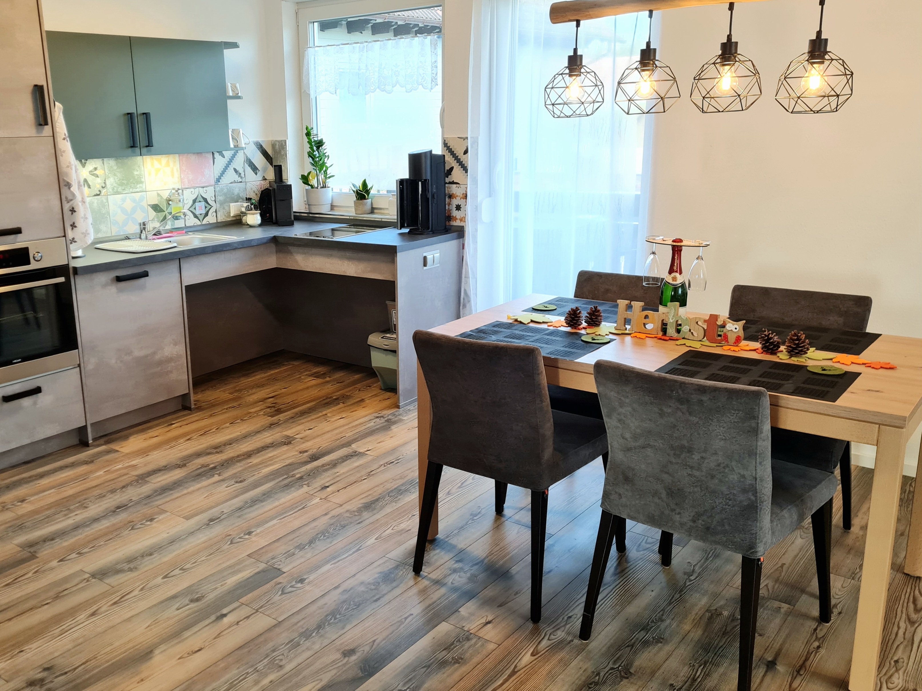 Rollstuhlgerechte Unterkunft - Barrierefreiheit-Merkmale: Für Gäste mit Gehbehinderung oder Rollstuhlfahrer - Schwarzwald - Offener Wohn- und Essbereich mit moderner Küche, Esstisch und stilvollen Hängeleuchten. Voll ausgestattete Küche in einer Ferienwohnung mit viel Tageslicht und gemütlichem Essplatz. - Pension Alter Hirsch - Ferienwohnung Buche