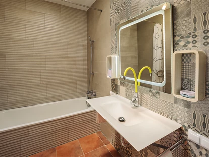 Rollstuhlgerechte Unterkunft - Unterkunftsart: Ferienhaus - Das Badezimmer vom Schlafzimmer Nr 1 mit Badewanne, beleuchteten Spiegel und gelb-grünen biegsamen Wasserhahn. - Poolvilla mit phantastischem Ausblick - mit Pool Lifter