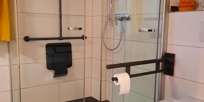 Rollstuhlgerechte Unterkunft - Oberbayern - befahrbare Falttürdusche mit Haltegriffen und Duschsitz, Toilette mit hochklappbaren Haltegriffen - Ferienwohnungen Weberhof