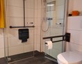 Rollstuhl-Urlaub: befahrbare Falttürdusche mit Haltegriffen und Duschsitz, Toilette mit hochklappbaren Haltegriffen - Ferienwohnungen Weberhof