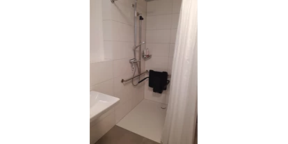 Rollstuhlgerechte Unterkunft - Pflegebett - Die stufenlose Dusche hat eine klappbaren Sitz und eine Reling. Das Waschbecken ist unterfahrbar und hat einen Spiegel in Sizhöhe. - Rolli Oase Ostseeresort Olpenitz (Kappeln)