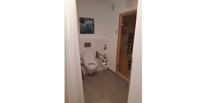 Rollstuhlgerechte Unterkunft - Pflegebett - Toilette mit hochklappbaren Griffen beidseits. Rechts die Infrarotkabine. - Rolli Oase Ostseeresort Olpenitz (Kappeln)