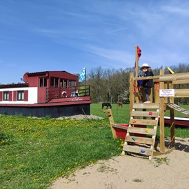 Rollstuhl-Urlaub: Blick von der Terrasse auf das Filmschiff ERBSE und den Spielplatz nur für das Erdhaus und das Filmschiff - Erdhausapartment WEST