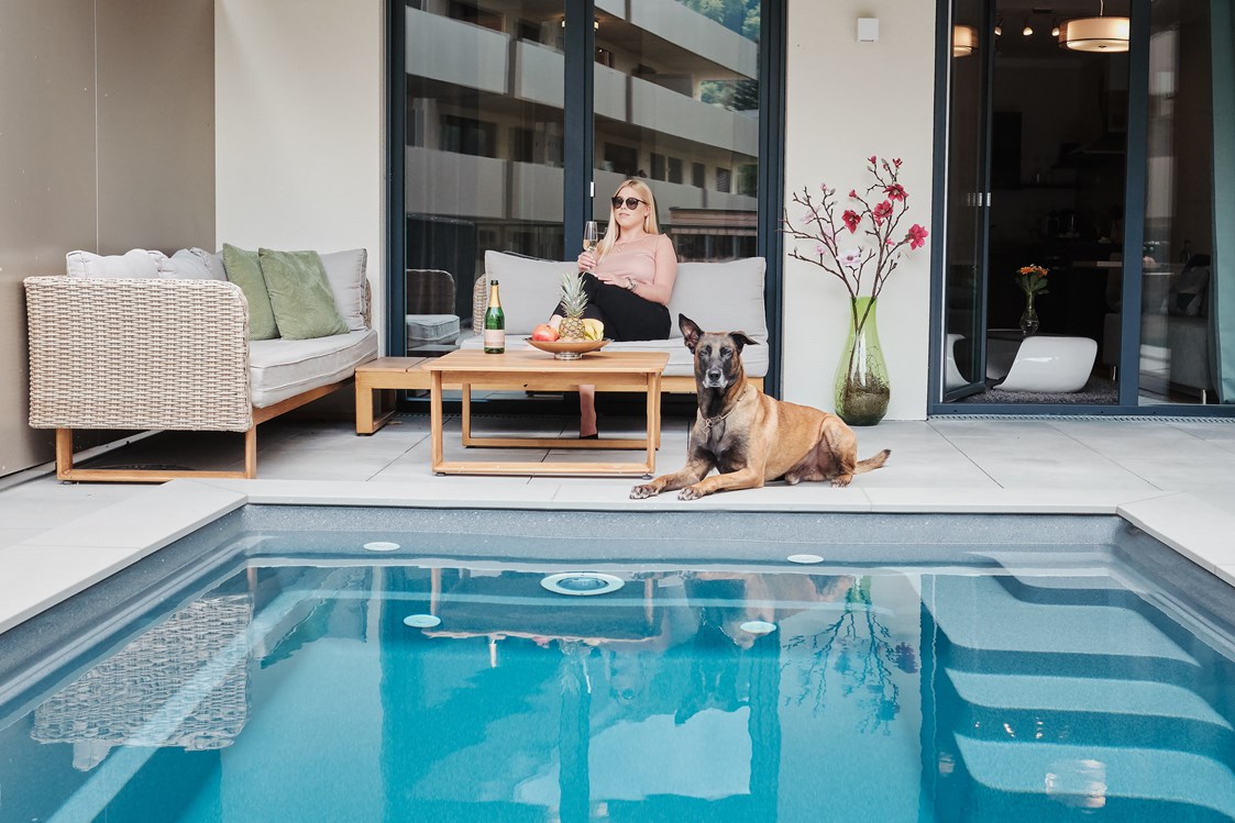 Rollstuhl-Urlaub: Das Bild ist aus unserer Poolsuite Ferdinand - P01.
Nur dieses Apartment hat einen Pool.
Auf dem Foto sitzt eine Frau mit Ihrem Hund auf der Terrasse vor dem Pool. - Kaiserapartments - Wohnpark Graz Gösting